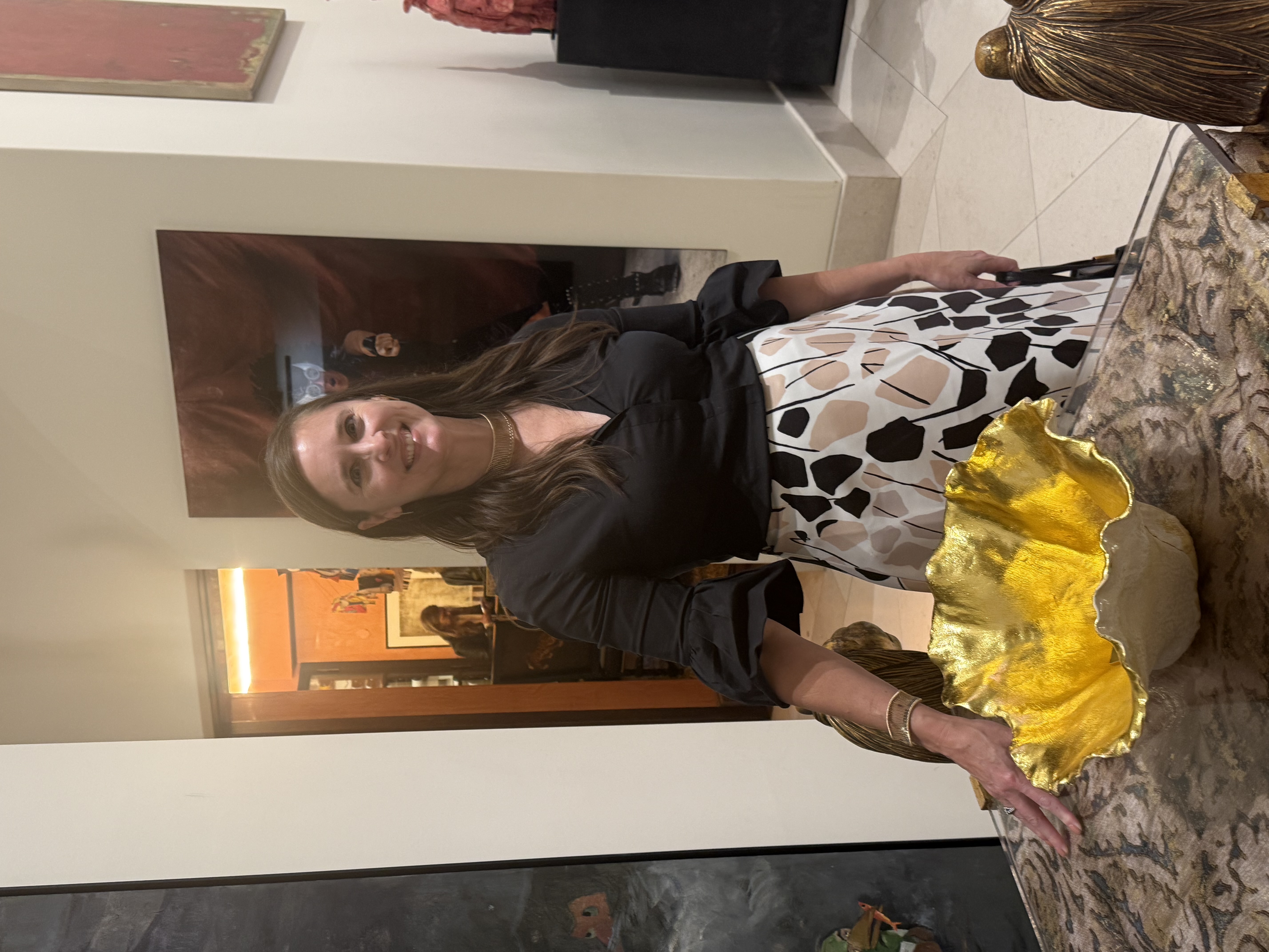 Rachel Rose smiling beside one of her gold-leafed ceramic bowls at a gallery exhibition